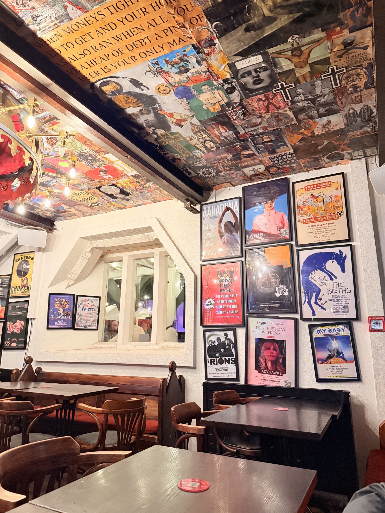 Posters, tables, and the ceiling collage inside The Church Pub