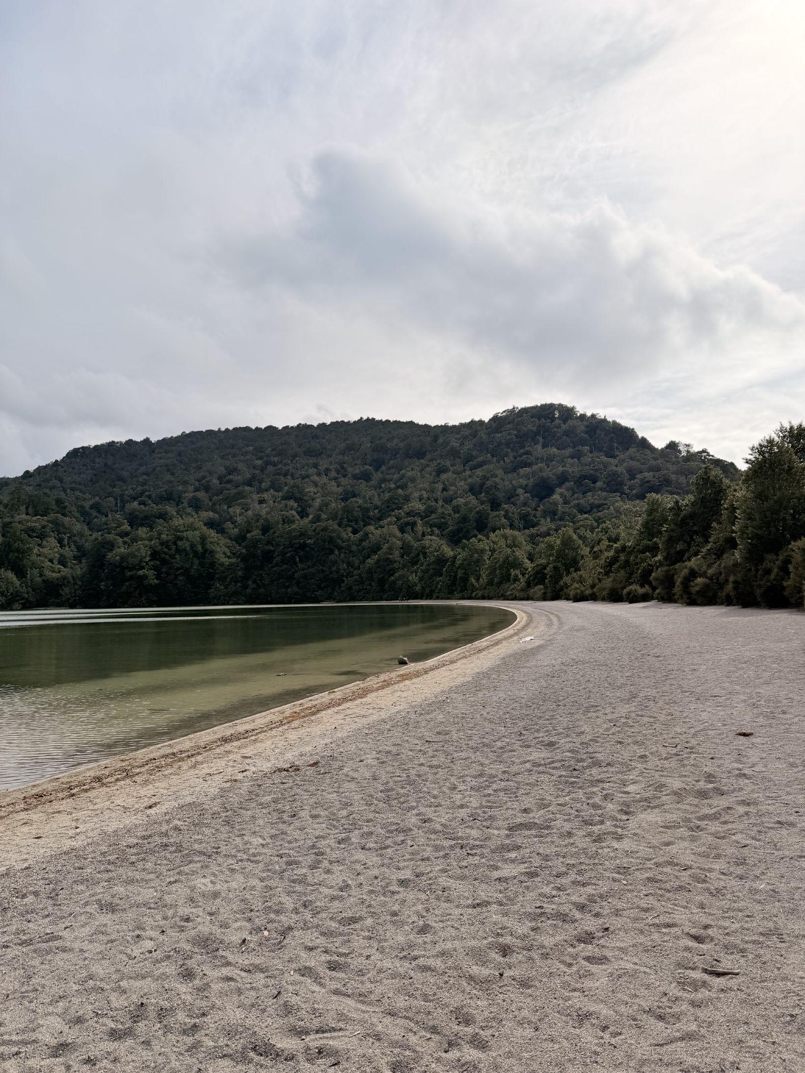 Sandy beach curving along the shoreline of Lake Rotopounamu with bush-covered hills behind